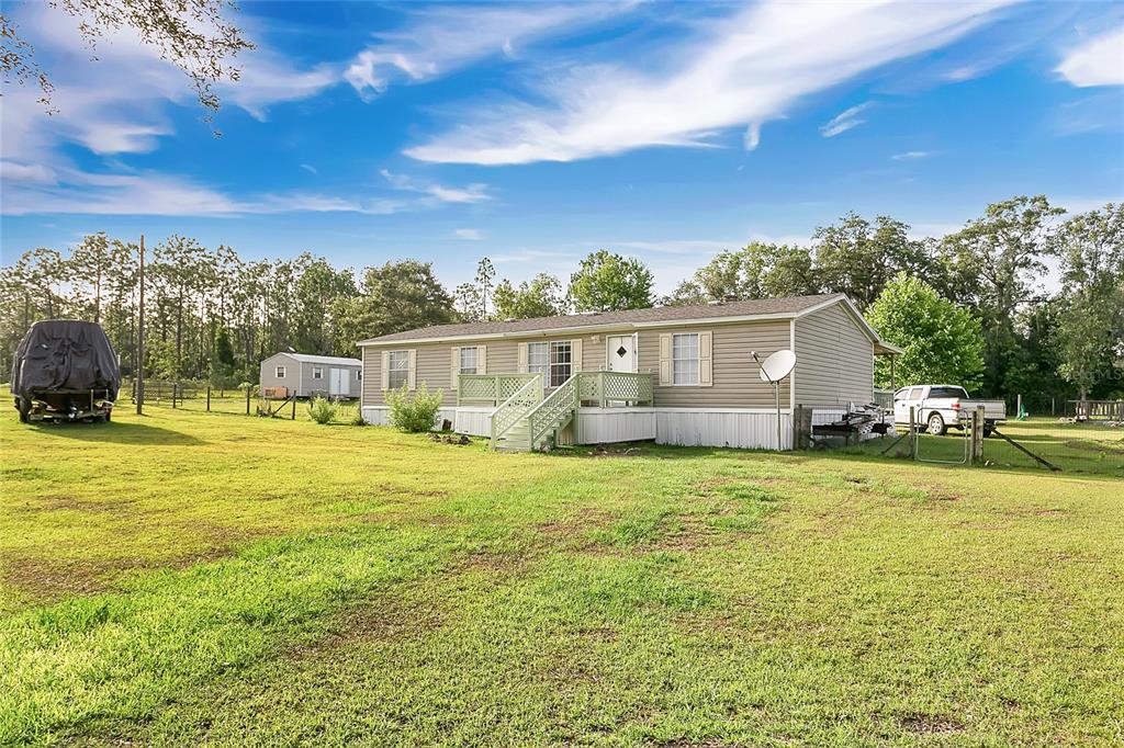 A single-story manufactured home with light siding, a front deck, and a large grassy yard — 12531 NE 18TH STREET, WILLISTON, FL
