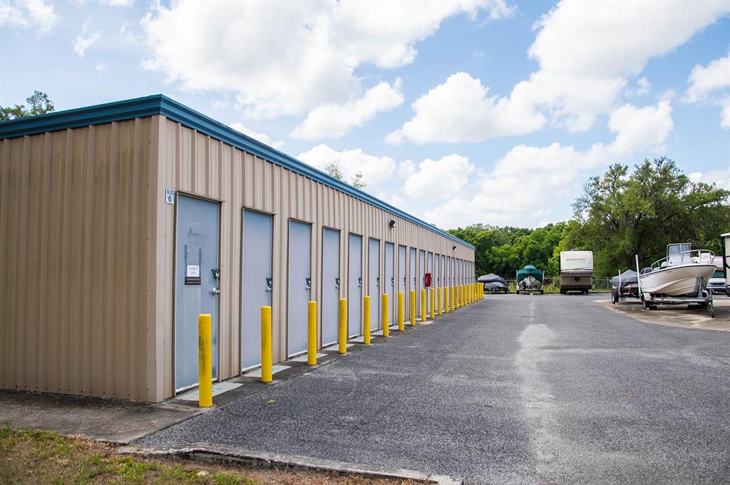 A long, tan metal storage building with multiple doors sits beside an outdoor parking area — 16881 SW ARCHER ROAD, ARCHER, FL