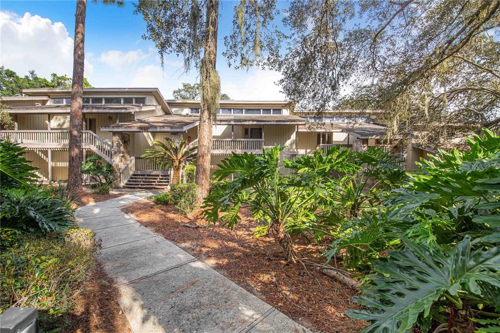 A concrete walkway leads to the entrance of a multi-level house with wood siding — 163 PALM VIEW COURT UNIT 3483/4, HAINES CITY, FL