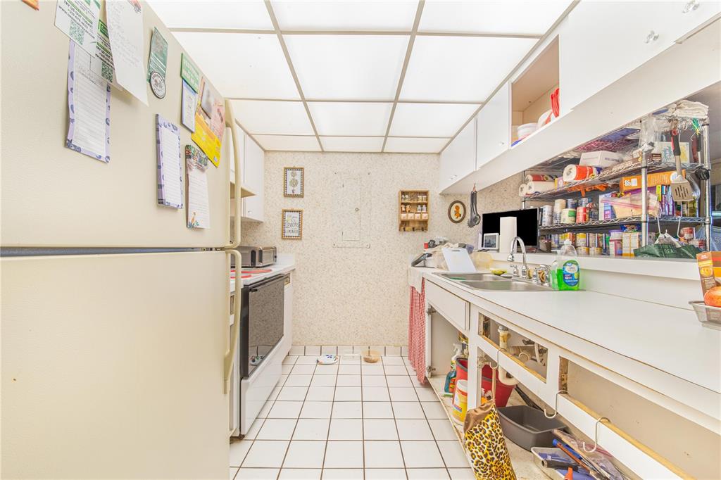 A galley kitchen features white appliances, tiled floors, open lower cabinets, and a drop ceiling — 163 PALM VIEW COURT UNIT 3483/4, HAINES CITY, FL