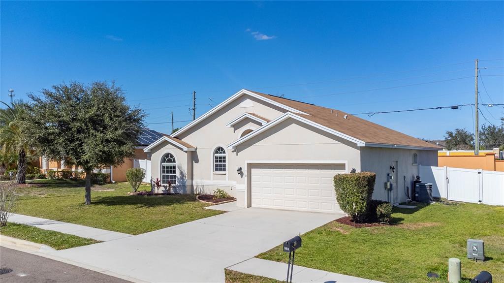 A single-story suburban house with a beige stucco exterior, a two-car garage, and a lawn — 518 HIGHLAND MEADOWS STREET, DAVENPORT, FL