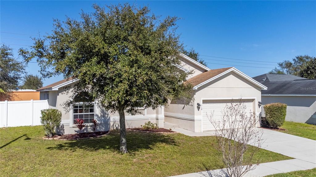 A single-story house with a beige exterior, a two-car garage, and a large front tree — 518 HIGHLAND MEADOWS STREET, DAVENPORT, FL