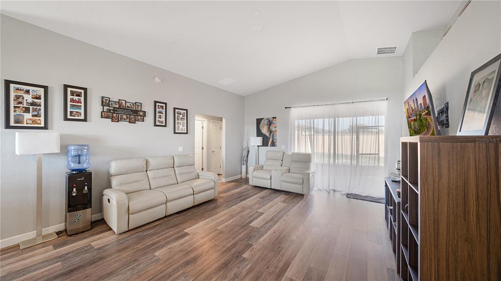 A living room features light-colored leather sofas, wood-look flooring, and a wall-mounted television — 518 HIGHLAND MEADOWS STREET, DAVENPORT, FL