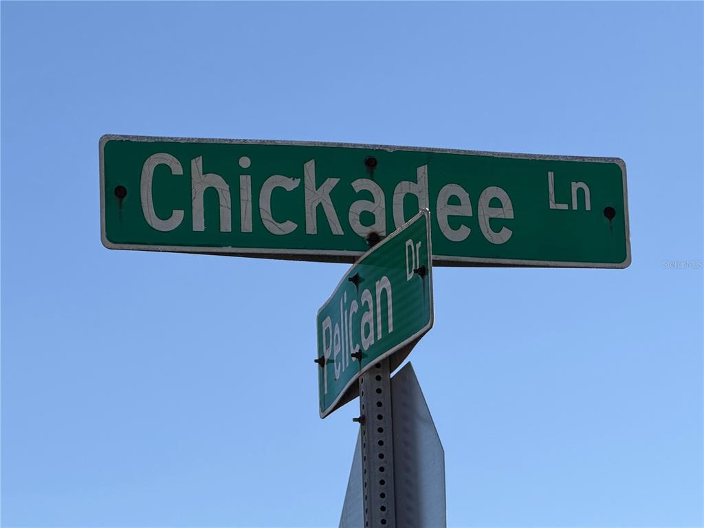 A street sign shows the intersection of Chickadee Lane and Pelican Drive against a blue sky — 7 & 9 CHICKADEE LANE, PLACIDA, FL