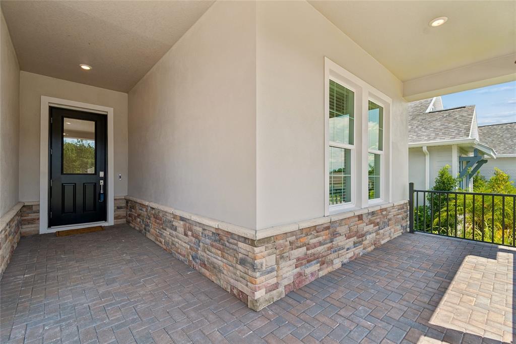 A covered porch features a black front door, stone veneer siding, and brick paver flooring — 4794 SOUTHERN VALLEY LOOP, BROOKSVILLE, FL