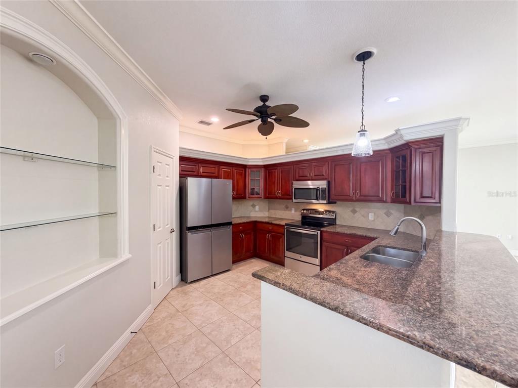 A kitchen features dark wood cabinets, granite countertops, stainless steel appliances, and a tiled floor — 4625 GARDEN AVENUE, SEBRING, FL