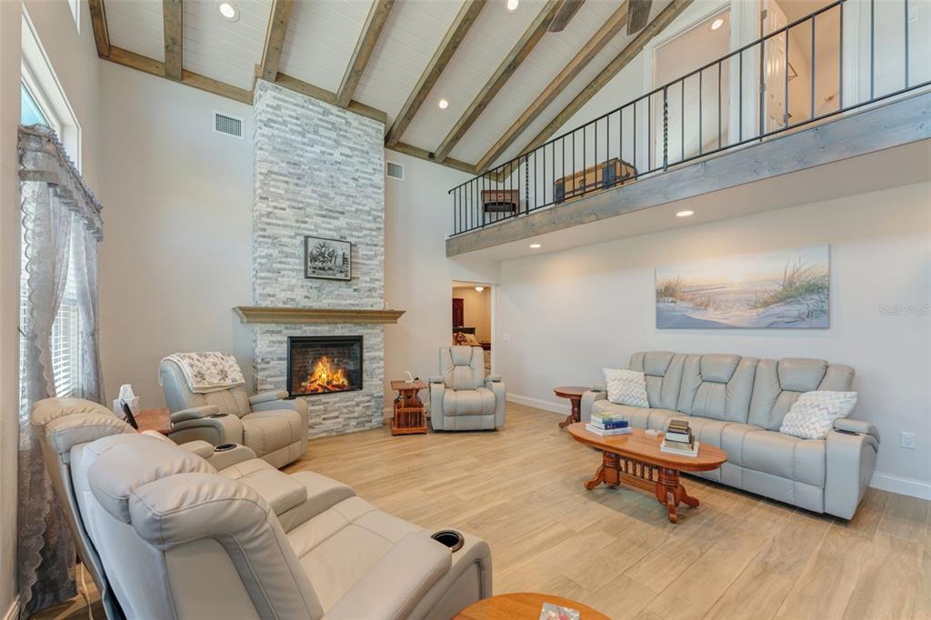 A living room with a stone fireplace, vaulted wood-beam ceiling, and a loft balcony — 3502 BAHIA VISTA STREET, SARASOTA, FL