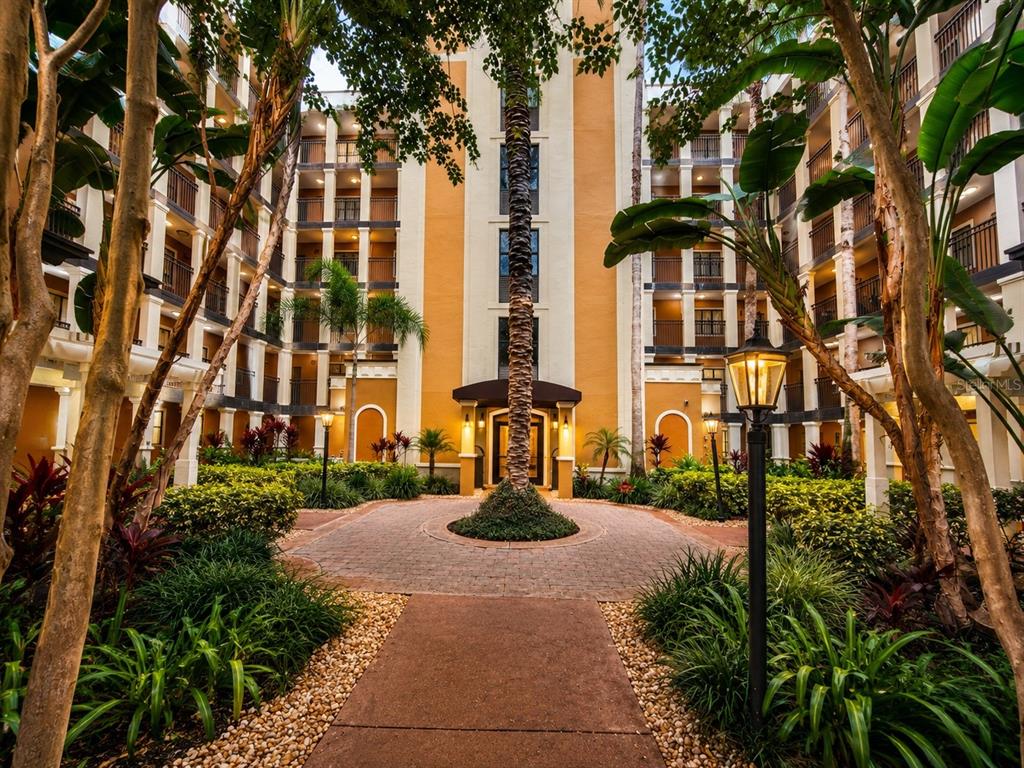 A paved walkway leads to the entrance of a multi-story apartment building with landscaped gardens — 12539 FLORIDAYS RESORT DRIVE UNIT 208D, ORLANDO, FL