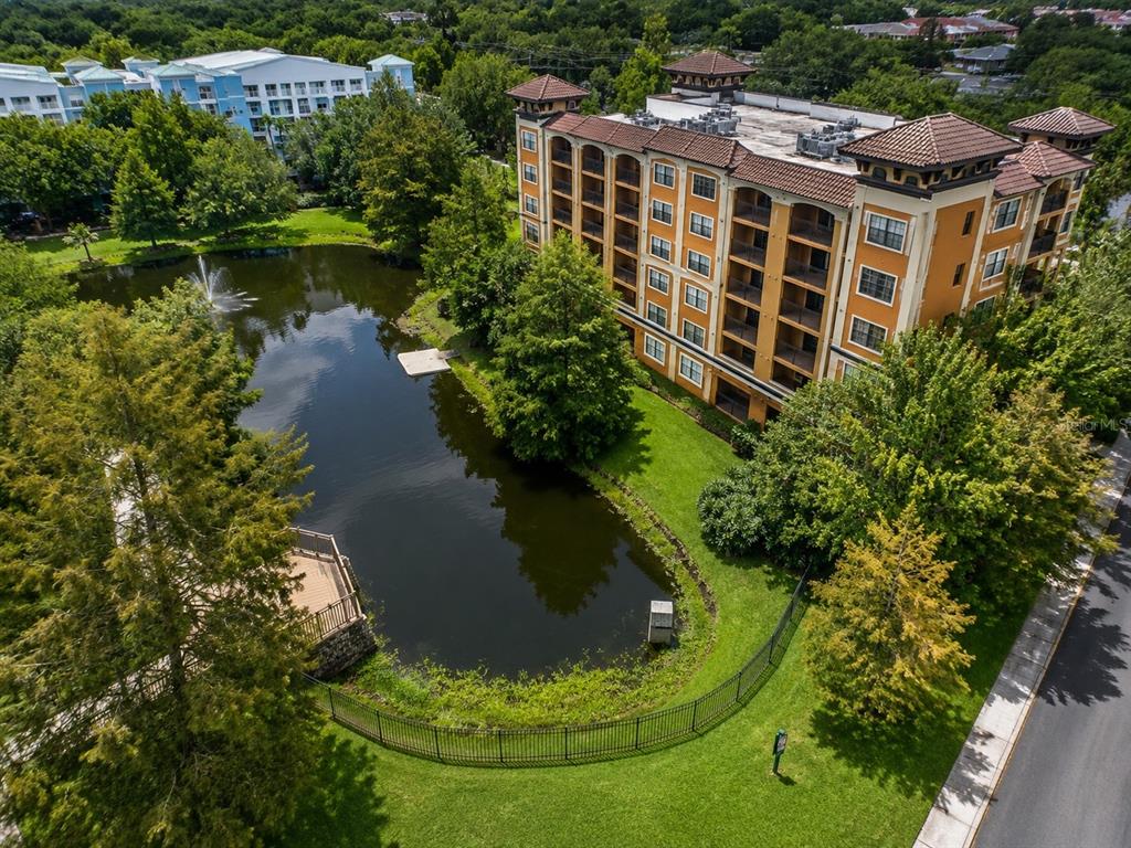 An aerial view of a multi-story apartment building next to a pond with a fountain — 12539 FLORIDAYS RESORT DRIVE UNIT 208D, ORLANDO, FL