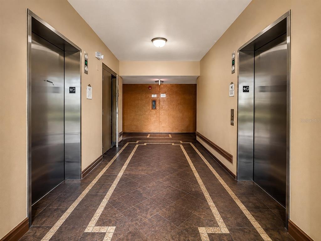 A hallway features two stainless steel elevators, tan walls, and patterned tile flooring — 12539 FLORIDAYS RESORT DRIVE UNIT 208D, ORLANDO, FL
