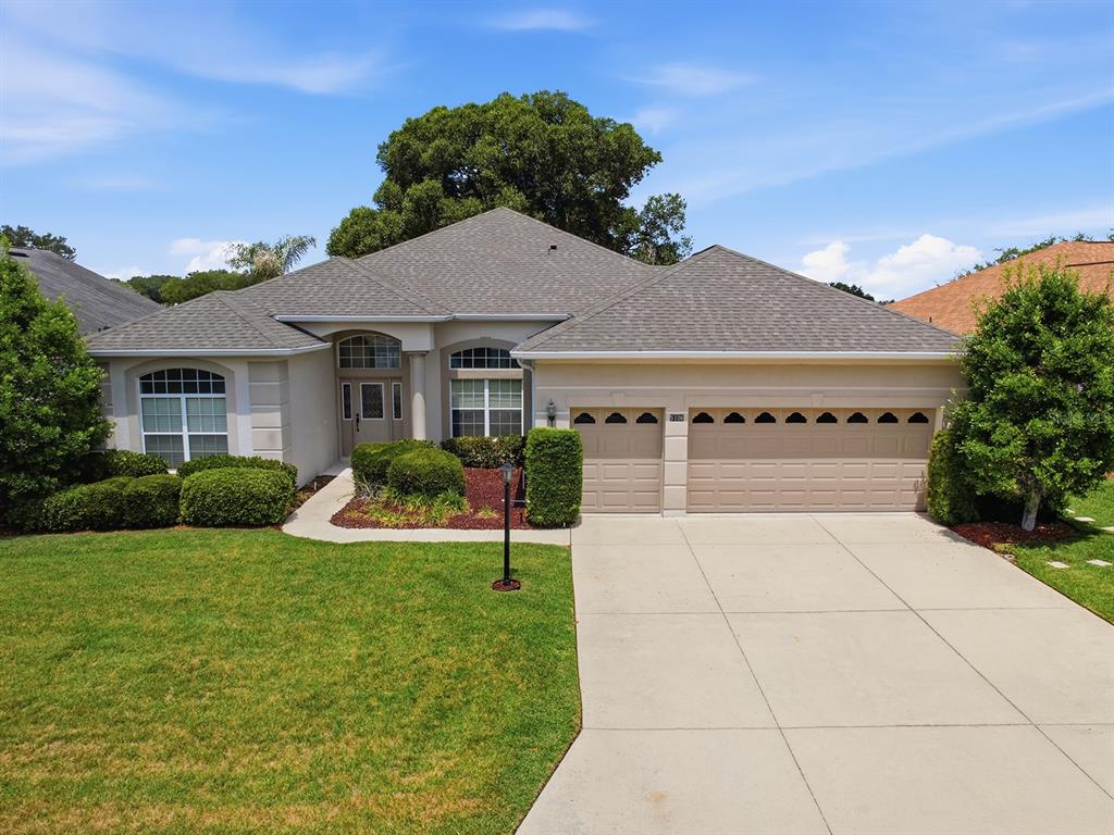 A single-story house with a beige stucco exterior, a gray shingled roof, and a driveway — 5106 CHANTICLEER DRIVE, LEESBURG, FL