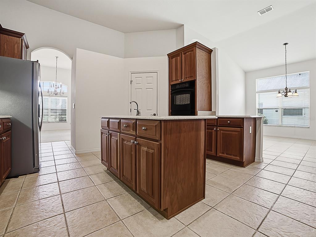 A kitchen features a central island, wood cabinetry, stainless steel appliances, and tiled flooring — 5106 CHANTICLEER DRIVE, LEESBURG, FL