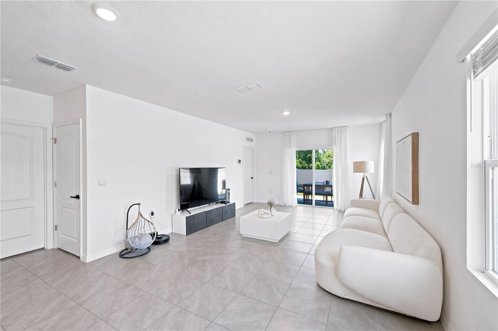 A bright living room features white walls, tile flooring, a white sofa, and a television — 2733 REDDISH EGRET BEND, HARMONY, FL