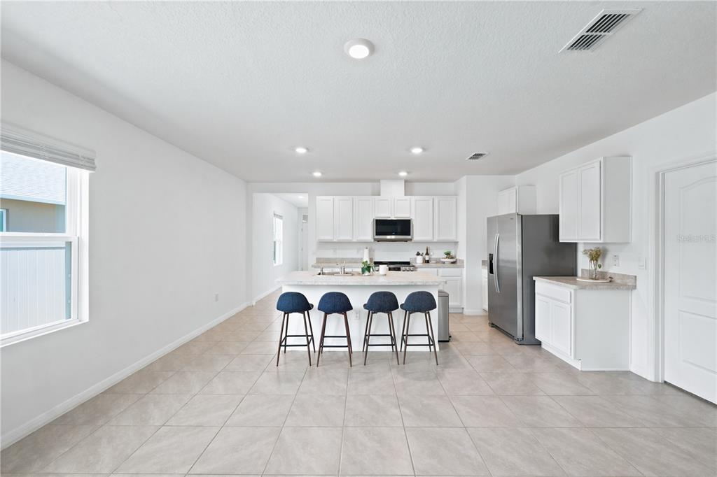 A kitchen with white cabinets, a central island with four stools, and tile flooring — 2733 REDDISH EGRET BEND, HARMONY, FL
