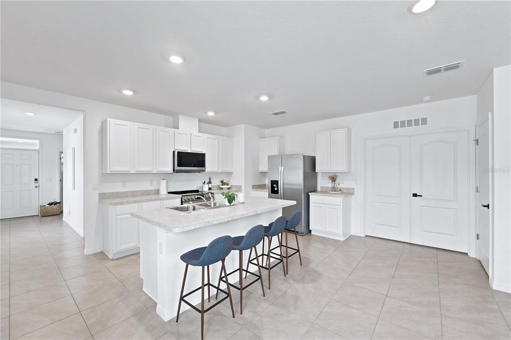 A bright kitchen features white cabinets, a central island with blue stools, and tile flooring — 2733 REDDISH EGRET BEND, HARMONY, FL