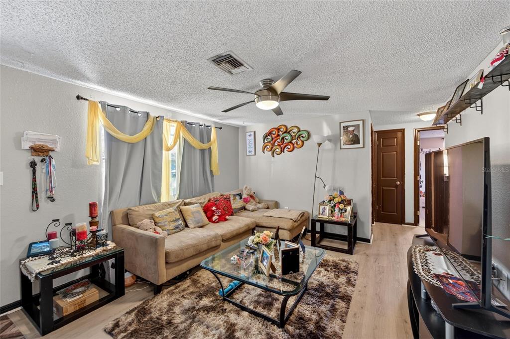 A living room features a sectional sofa, glass coffee table, ceiling fan, and wood-look flooring — 15821 ADOBE DRIVE, HUDSON, FL