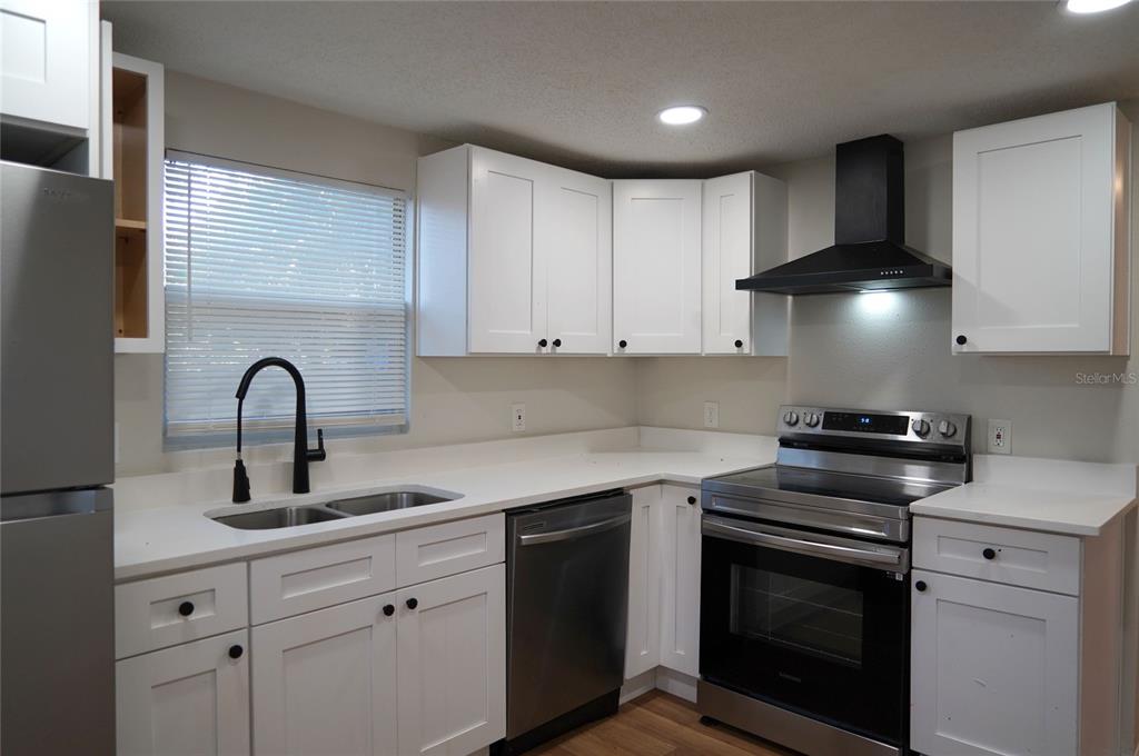 A kitchen features white cabinets, stainless steel appliances, a double sink, and light wood flooring — 4509 N 29TH STREET, TAMPA, FL