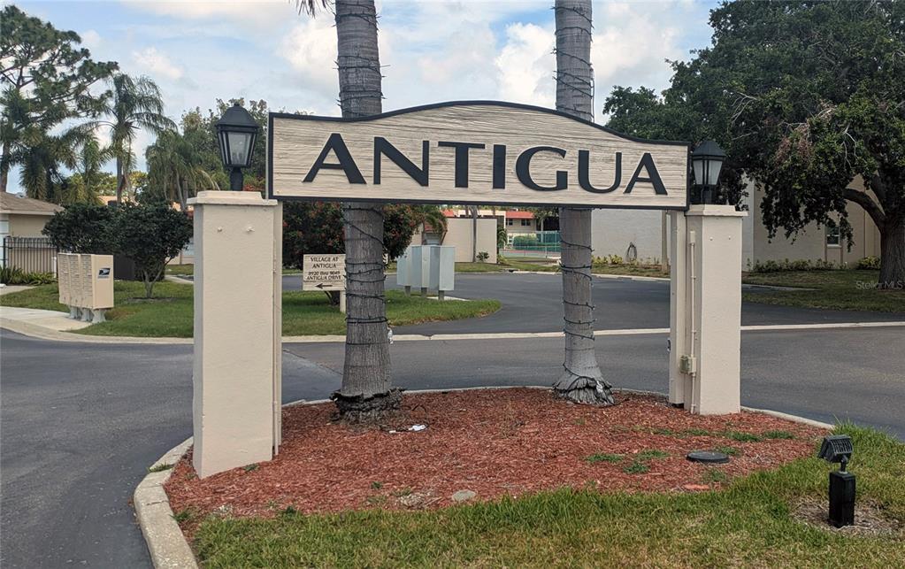 A sign reading Antigua stands between two palm trees at the entrance to a residential community — 9700 STARKEY ROAD UNIT 325, SEMINOLE, FL