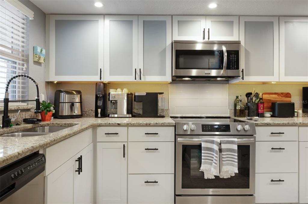 A kitchen features white cabinets with frosted glass, stainless steel appliances, and granite countertops — 9700 STARKEY ROAD UNIT 325, SEMINOLE, FL