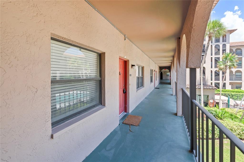 An outdoor apartment building walkway with a red door, windows, and a metal railing — 6150 GULFPORT BOULEVARD S UNIT 202, GULFPORT, FL