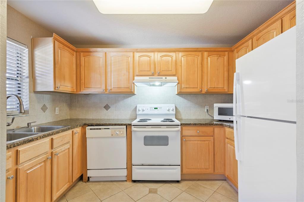 A kitchen features light wood cabinets, granite countertops, white appliances, and tiled flooring — 6150 GULFPORT BOULEVARD S UNIT 202, GULFPORT, FL