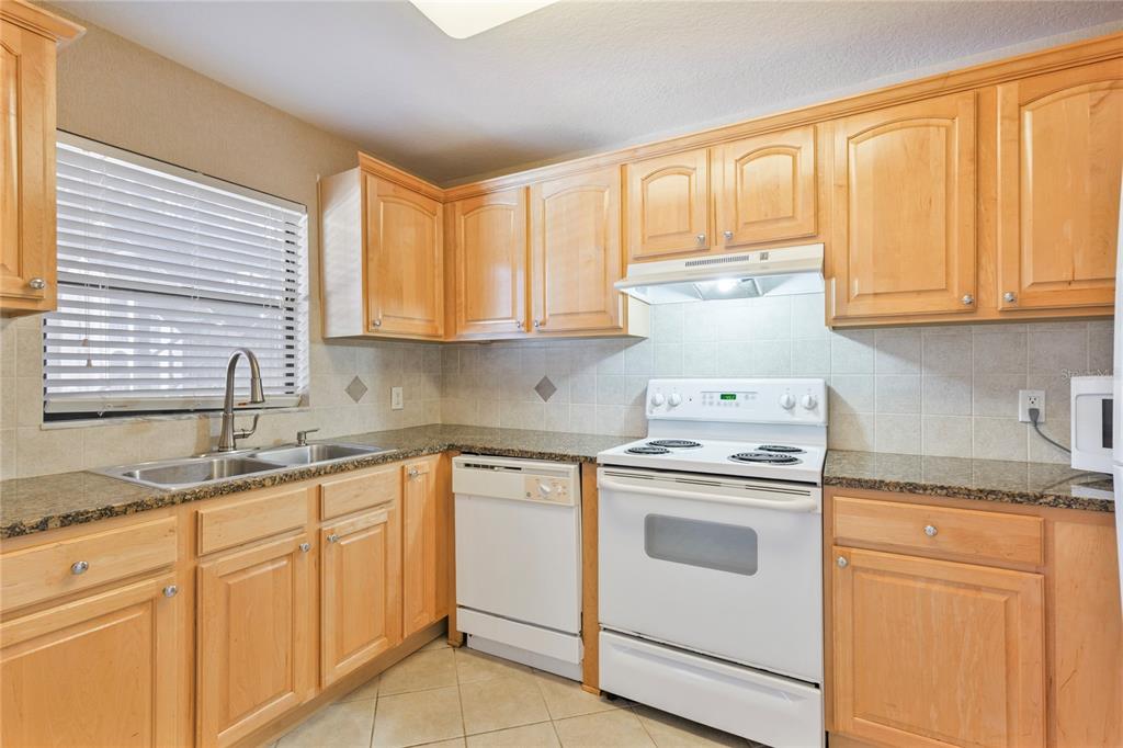 A kitchen with light wood cabinets, granite countertops, white appliances, and a double-basin sink — 6150 GULFPORT BOULEVARD S UNIT 202, GULFPORT, FL
