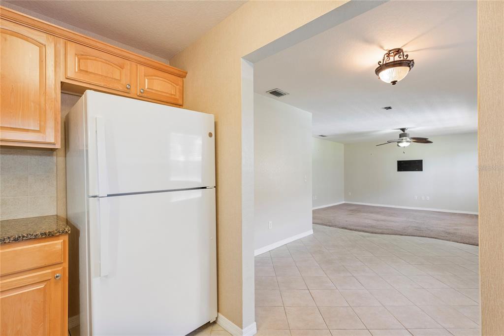A white refrigerator stands in a kitchen with wood cabinets next to a tiled living area — 6150 GULFPORT BOULEVARD S UNIT 202, GULFPORT, FL