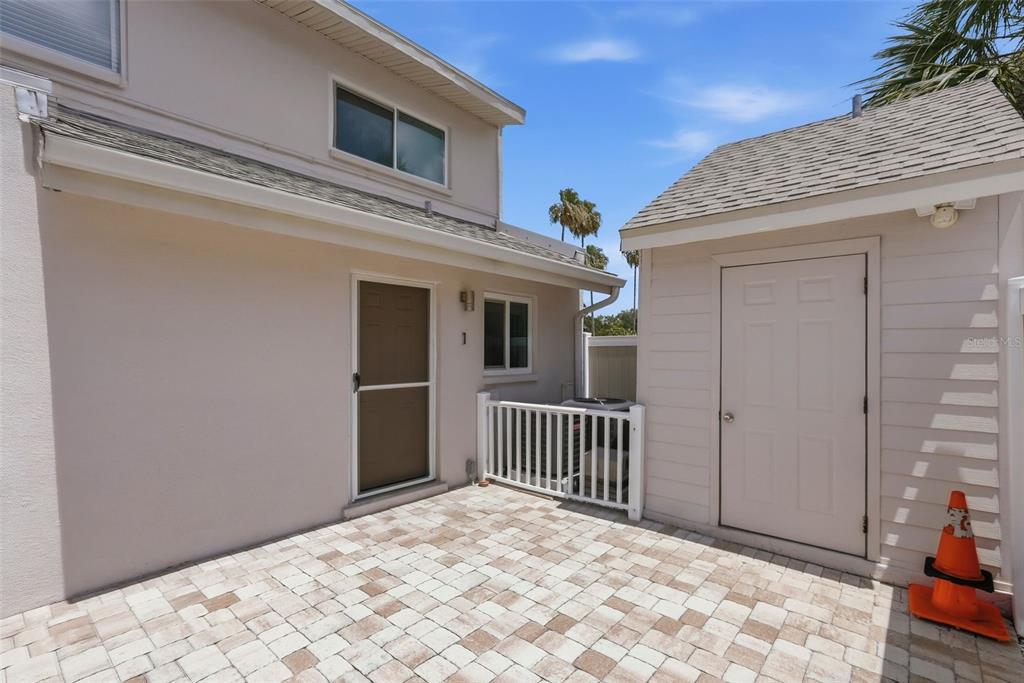 A paved patio sits between a two-story residential building and a small detached storage shed — 3120 BEACH BOULEVARD S UNIT 1, ST PETERSBURG, FL