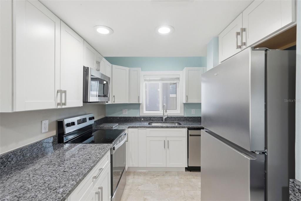 A kitchen features white cabinets, granite countertops, stainless steel appliances, and light blue walls — 3120 BEACH BOULEVARD S UNIT 1, ST PETERSBURG, FL