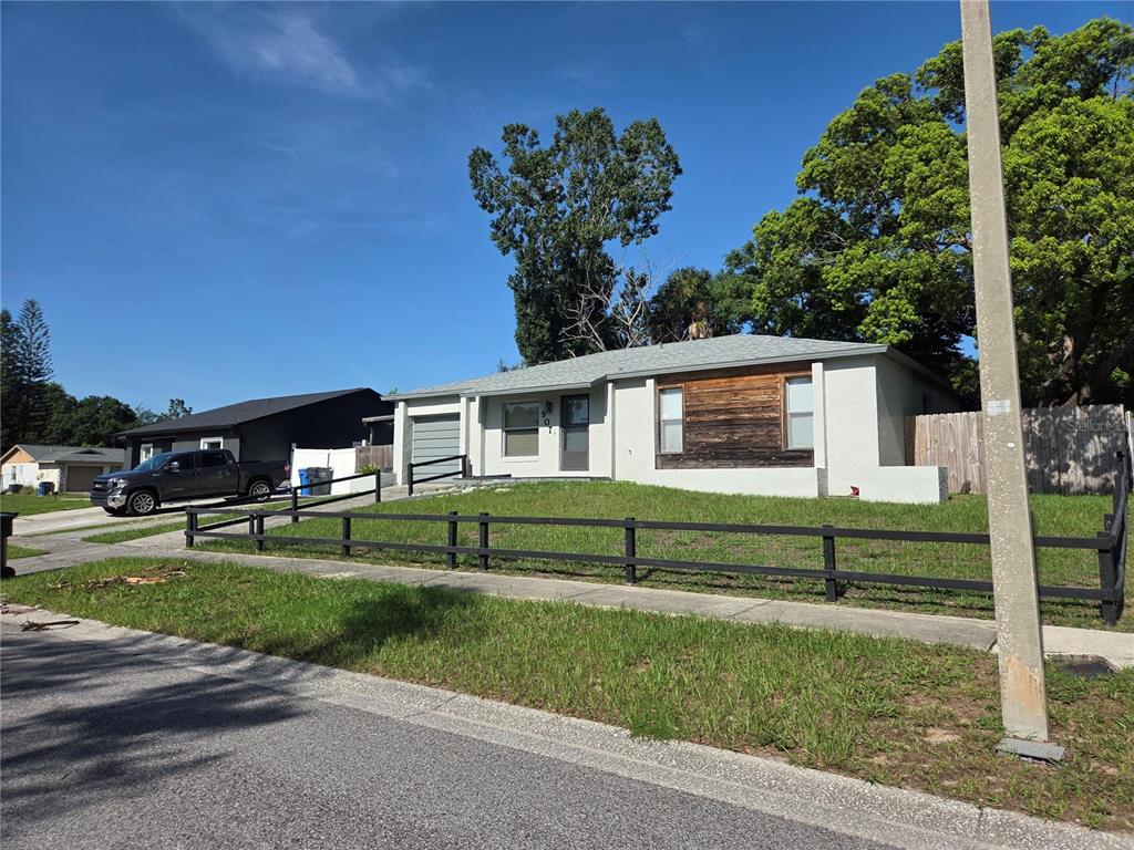 A single-story house with a light-colored exterior, wood accent wall, and a black fence — 907 CUTLER DRIVE, SEFFNER, FL