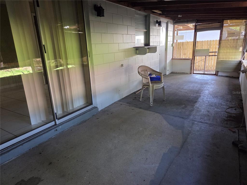 A covered concrete patio features a white block wall, a sliding glass door, and a chair — 907 CUTLER DRIVE, SEFFNER, FL