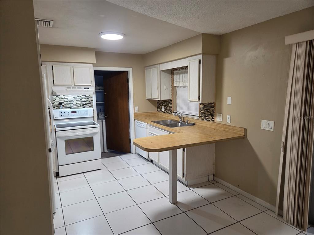 A kitchen features white cabinets, a wood-look countertop, white appliances, and light-colored floor tiles — 907 CUTLER DRIVE, SEFFNER, FL