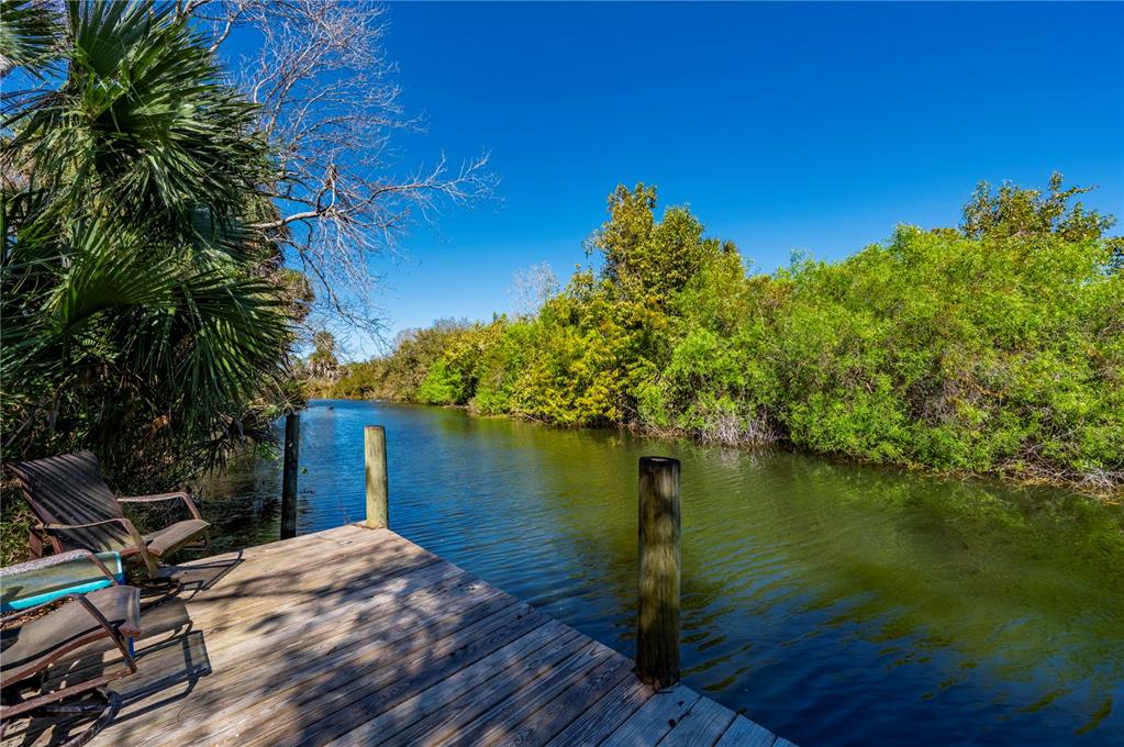 A wooden dock with chairs overlooks a narrow canal surrounded by lush green trees — 29505 JONES LOOP ROAD, PUNTA GORDA, FL
