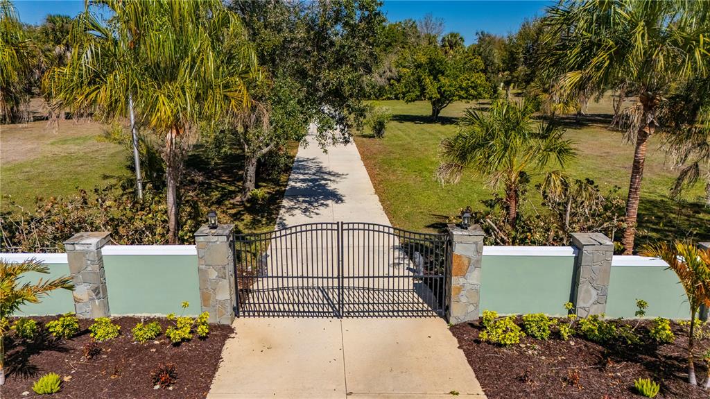 A metal gate with stone pillars opens to a concrete driveway on a grassy lot — 29505 JONES LOOP ROAD, PUNTA GORDA, FL