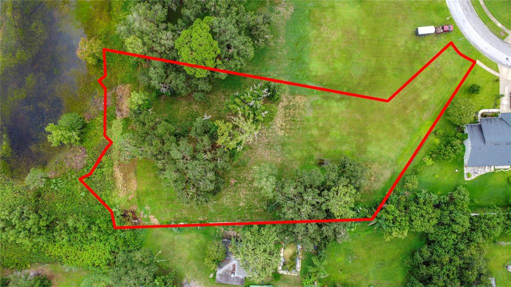 An aerial view shows a vacant, grassy lot outlined in red next to a lake — 4808 CALASANS AVENUE, ST CLOUD, FL