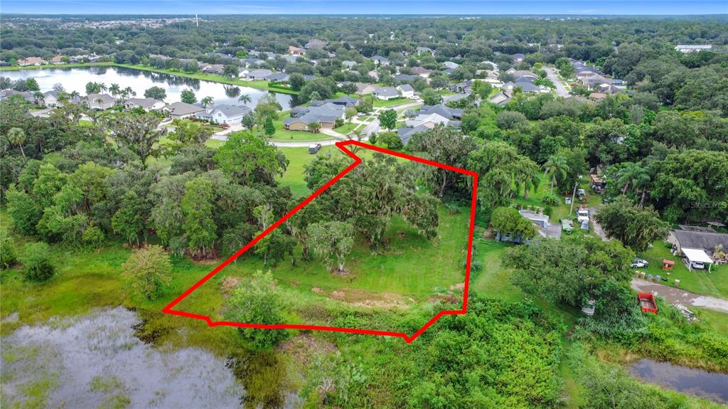 An aerial view shows a vacant, tree-covered lot outlined in red next to a lake — 4808 CALASANS AVENUE, ST CLOUD, FL