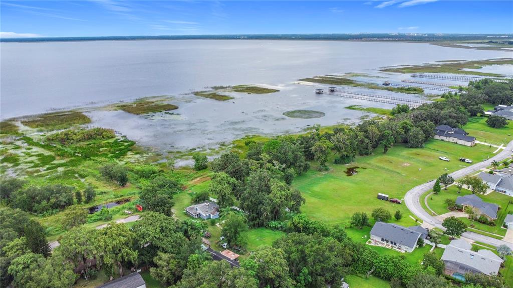 An aerial view shows a house nestled among trees near a large lake with docks — 4808 CALASANS AVENUE, ST CLOUD, FL