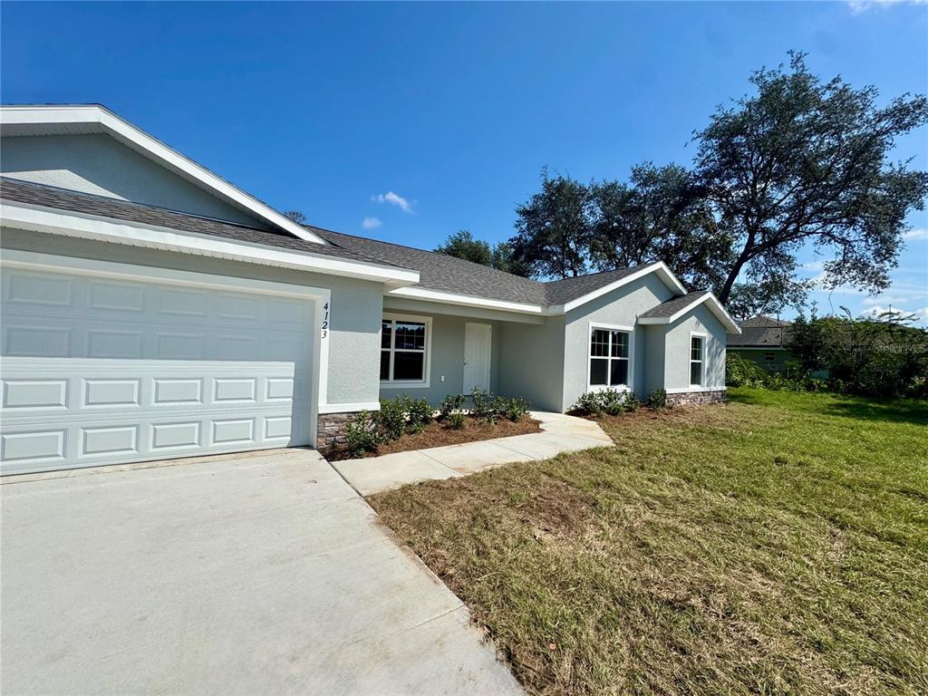 A single-story house exterior features a two-car garage, light-colored stucco walls, and a concrete walkway — 5513 SW 137TH COURT, OCALA, FL