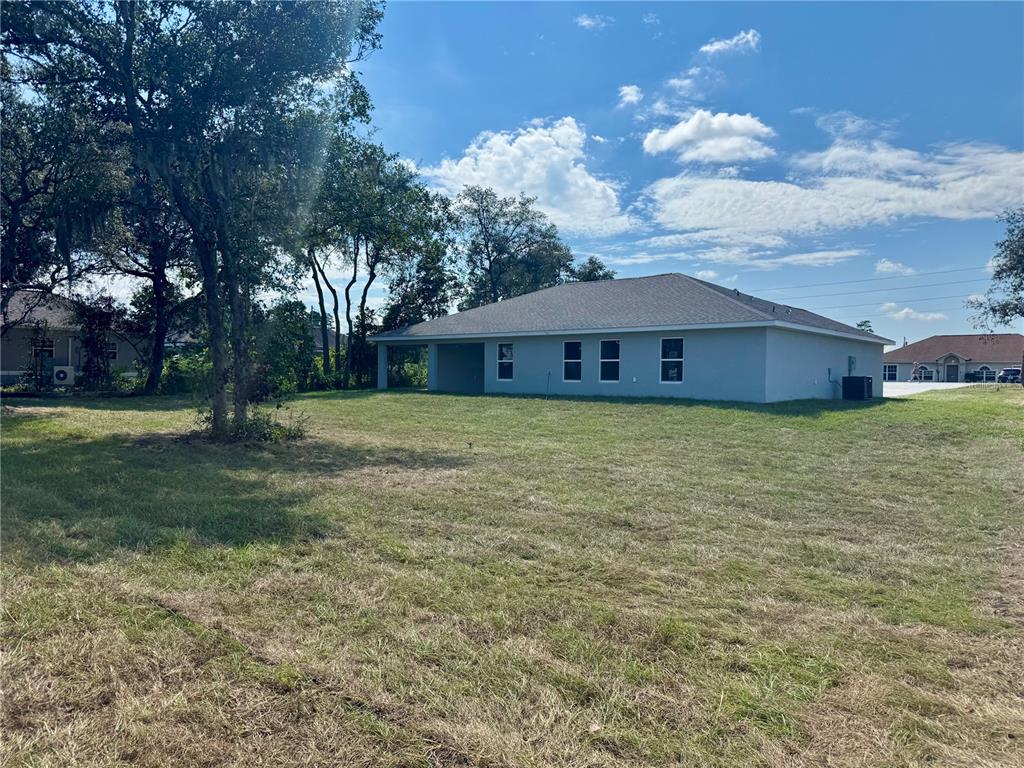 A view of the rear exterior of a single-story house with a large grassy yard — 5513 SW 137TH COURT, OCALA, FL