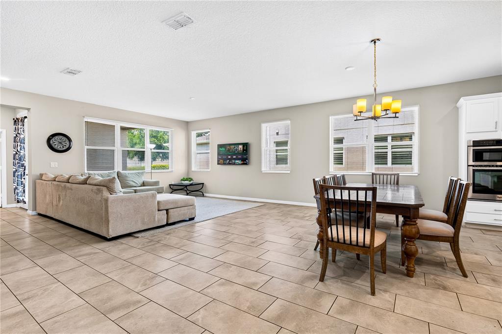 An open-concept living and dining area features tile flooring, a beige sectional, and wooden furniture — 13831 FARELLA ALLEY, WINDERMERE, FL