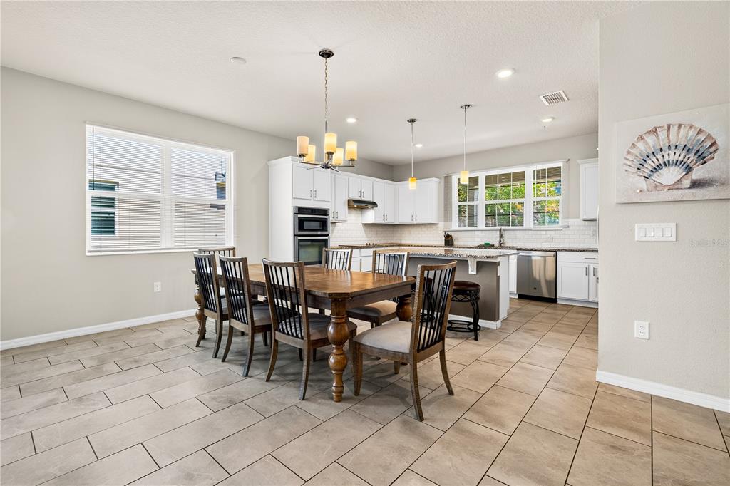 A dining area with a wooden table and chairs sits adjacent to a white kitchen — 13831 FARELLA ALLEY, WINDERMERE, FL