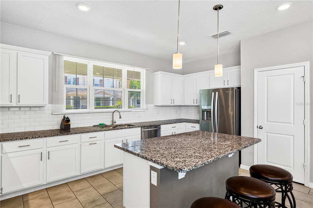 A kitchen features white cabinetry, granite countertops, a center island, and stainless steel appliances — 13831 FARELLA ALLEY, WINDERMERE, FL