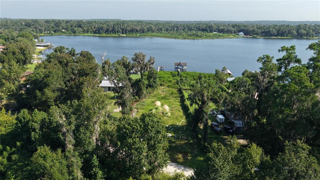 An aerial view shows a grassy, tree-lined lot leading to a lake with a dock — 201 FLORADANDY ROAD, HAWTHORNE, FL