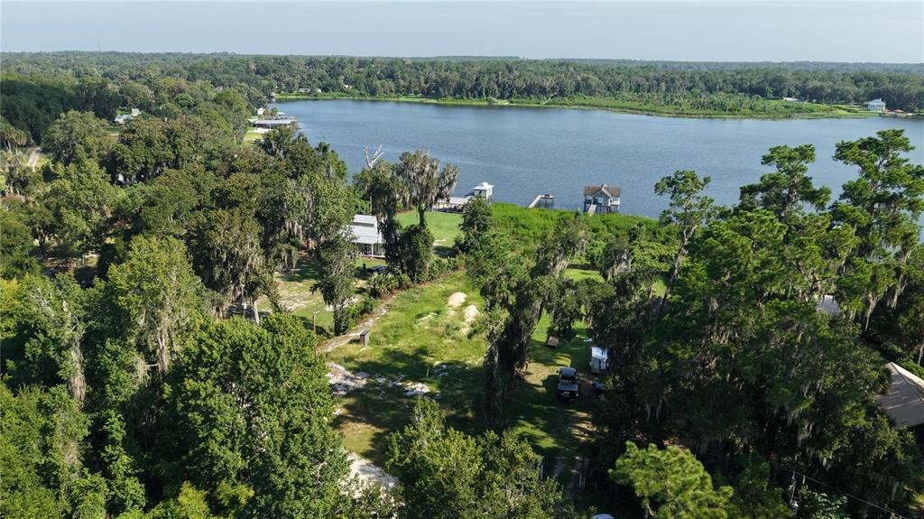 An aerial view shows a grassy lot with trees leading to a lake with docks — 201 FLORADANDY ROAD, HAWTHORNE, FL
