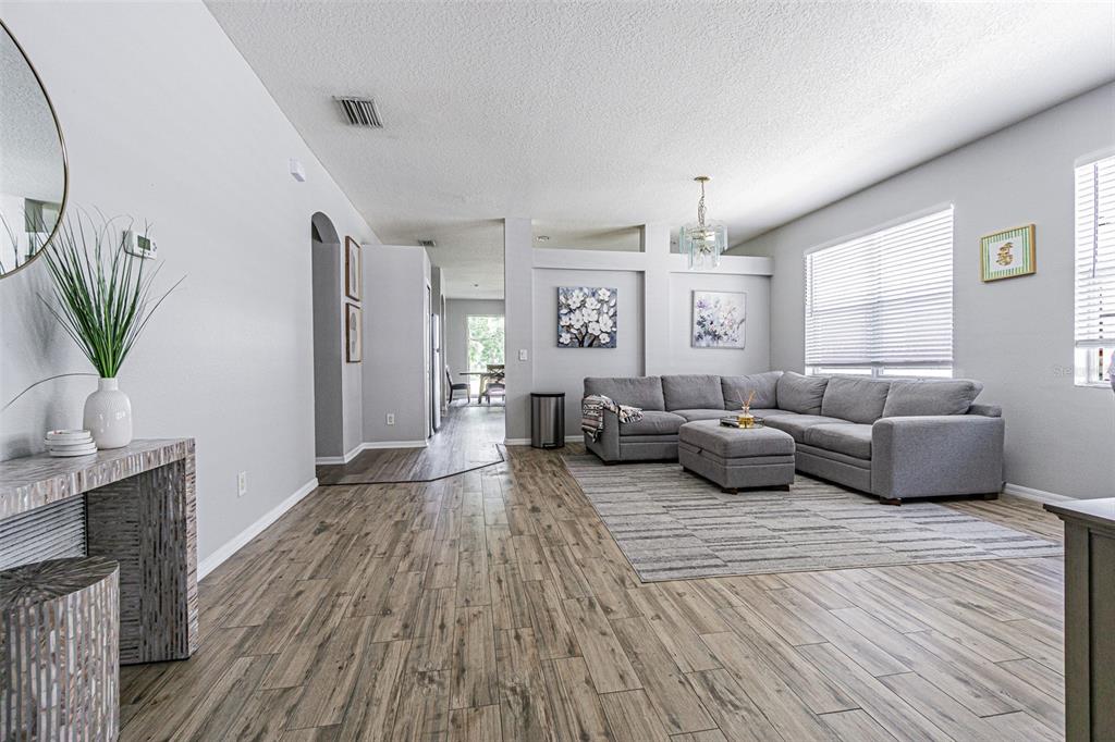 A living room features a grey sectional sofa, wood-look flooring, and a television on a console — 13016 TERRACE BROOK PLACE, TEMPLE TERRACE, FL