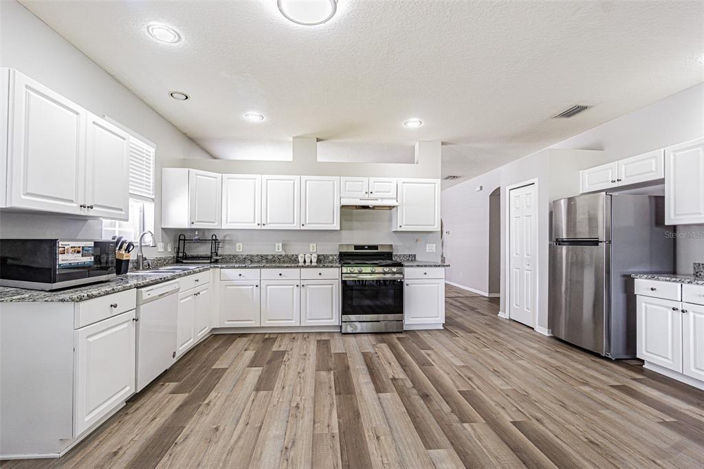 A kitchen features white cabinets, granite countertops, stainless steel appliances, and wood-look flooring — 13016 TERRACE BROOK PLACE, TEMPLE TERRACE, FL