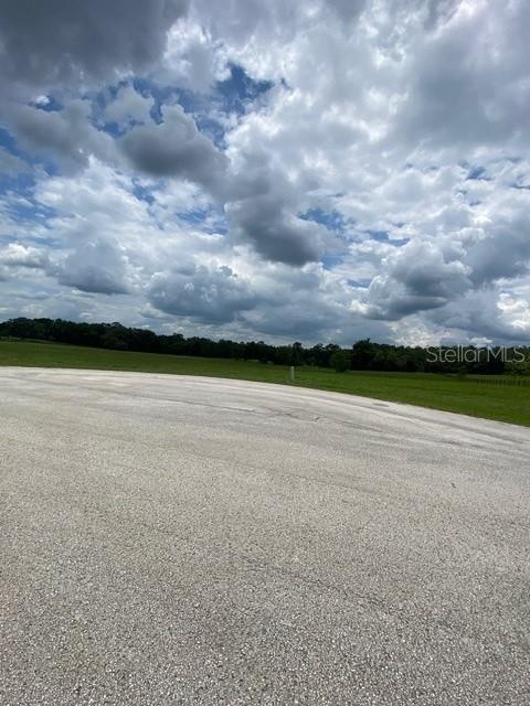 A paved area sits in the foreground before a large, grassy field under cloudy skies — 5698 QUICKSILVER, FLORAL CITY, FL