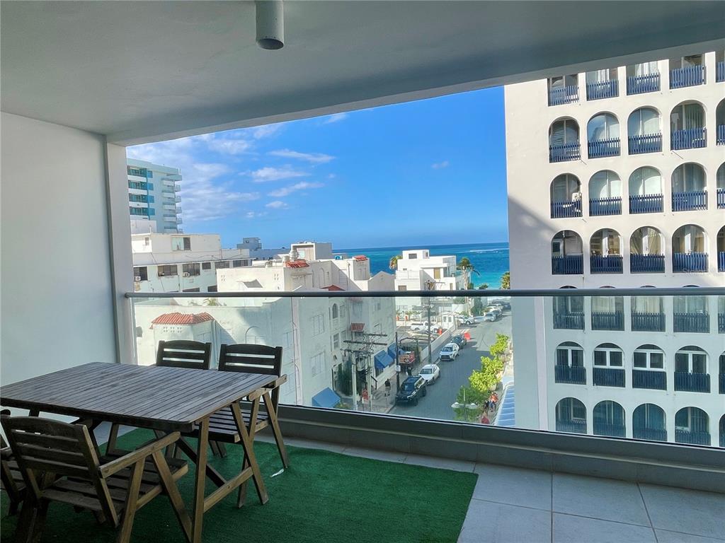 A balcony with a wooden table and chairs overlooks a street, buildings, and the ocean — 1124 ASHFORD AVENUE UNIT 6A, SAN JUAN, PR