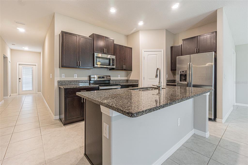 A kitchen features dark wood cabinets, granite countertops, a center island, and stainless steel appliances — 13009 MAJESTIC GARDEN LANE, RIVERVIEW, FL