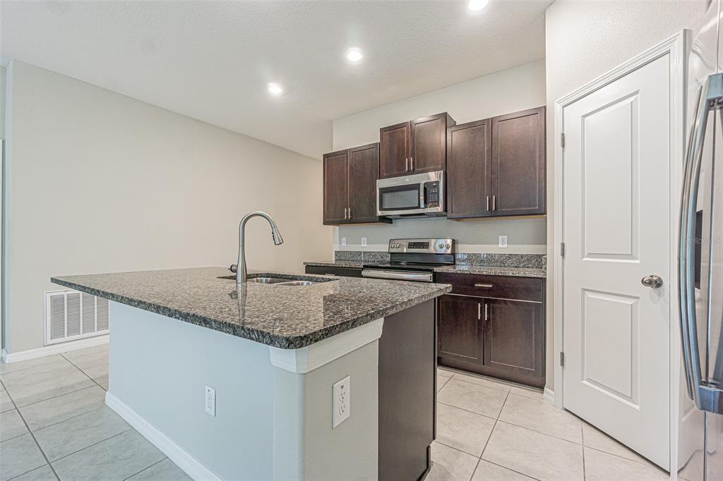 A kitchen with dark wood cabinets, granite countertops, a center island, and stainless steel appliances — 13009 MAJESTIC GARDEN LANE, RIVERVIEW, FL